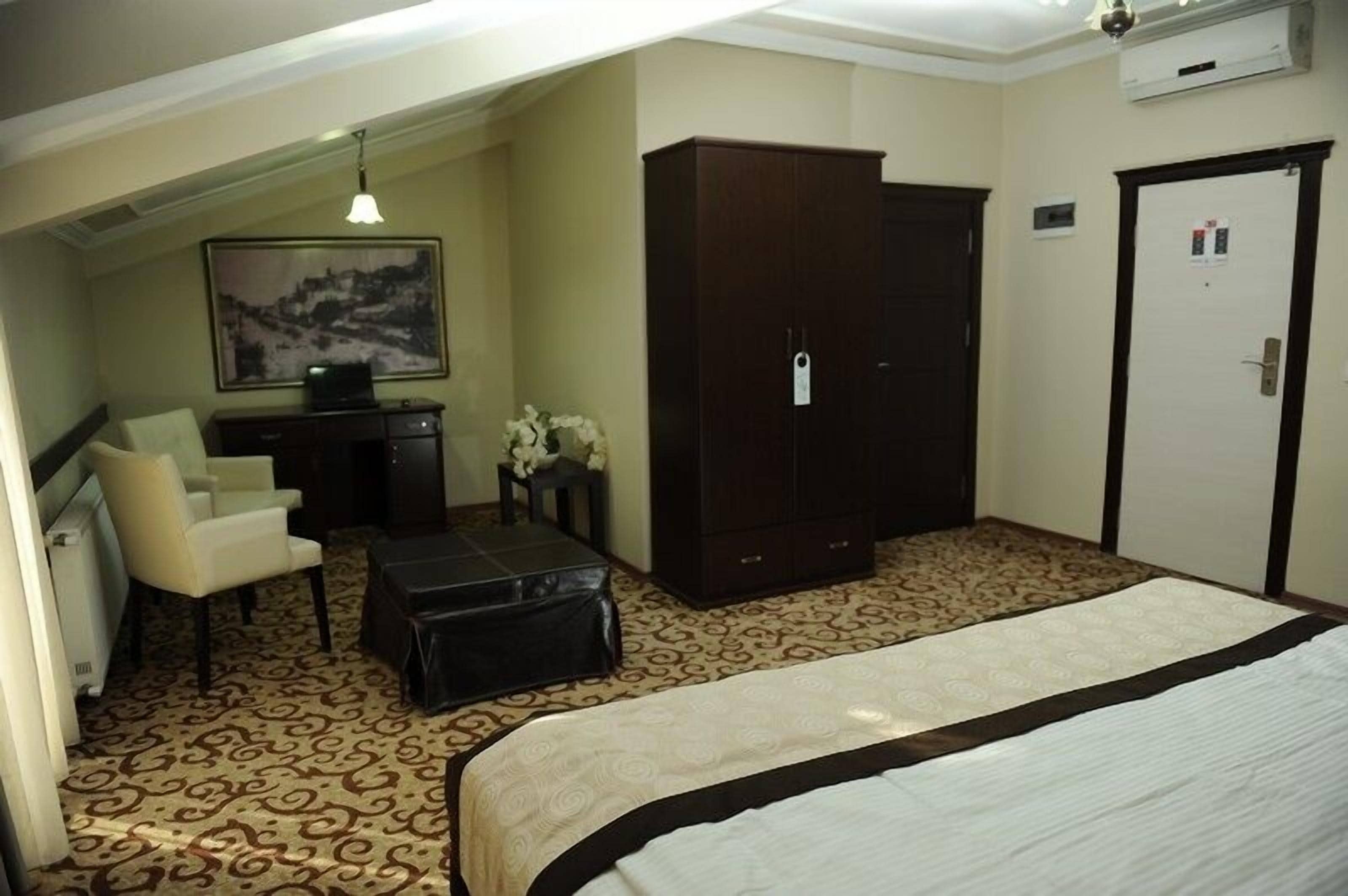 Habitación de hotel con cama, escritorio y silla, armario, una mesita con flores y un cuadro en la pared.