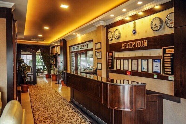 Zona de recepción con mostrador, un reloj y un letrero de restaurante.