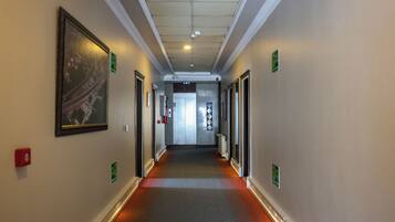 A corridor with doors on both sides, emergency exit signs, and a fire alarm on the wall.