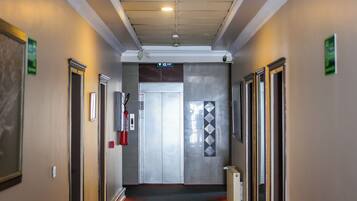 A hotel corridor with doors on both sides, a fire extinguisher, and an exit sign.