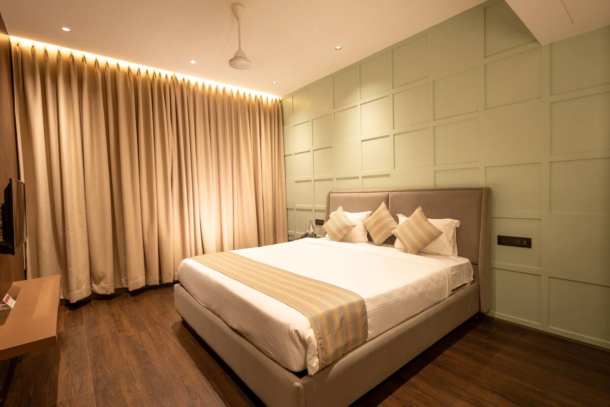 A large bed with a headboard, beige curtains, and a wooden floor.