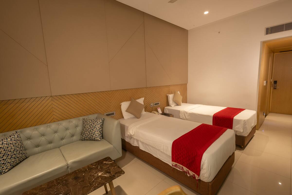 A hotel room with two single beds, a sofa, and a small table.