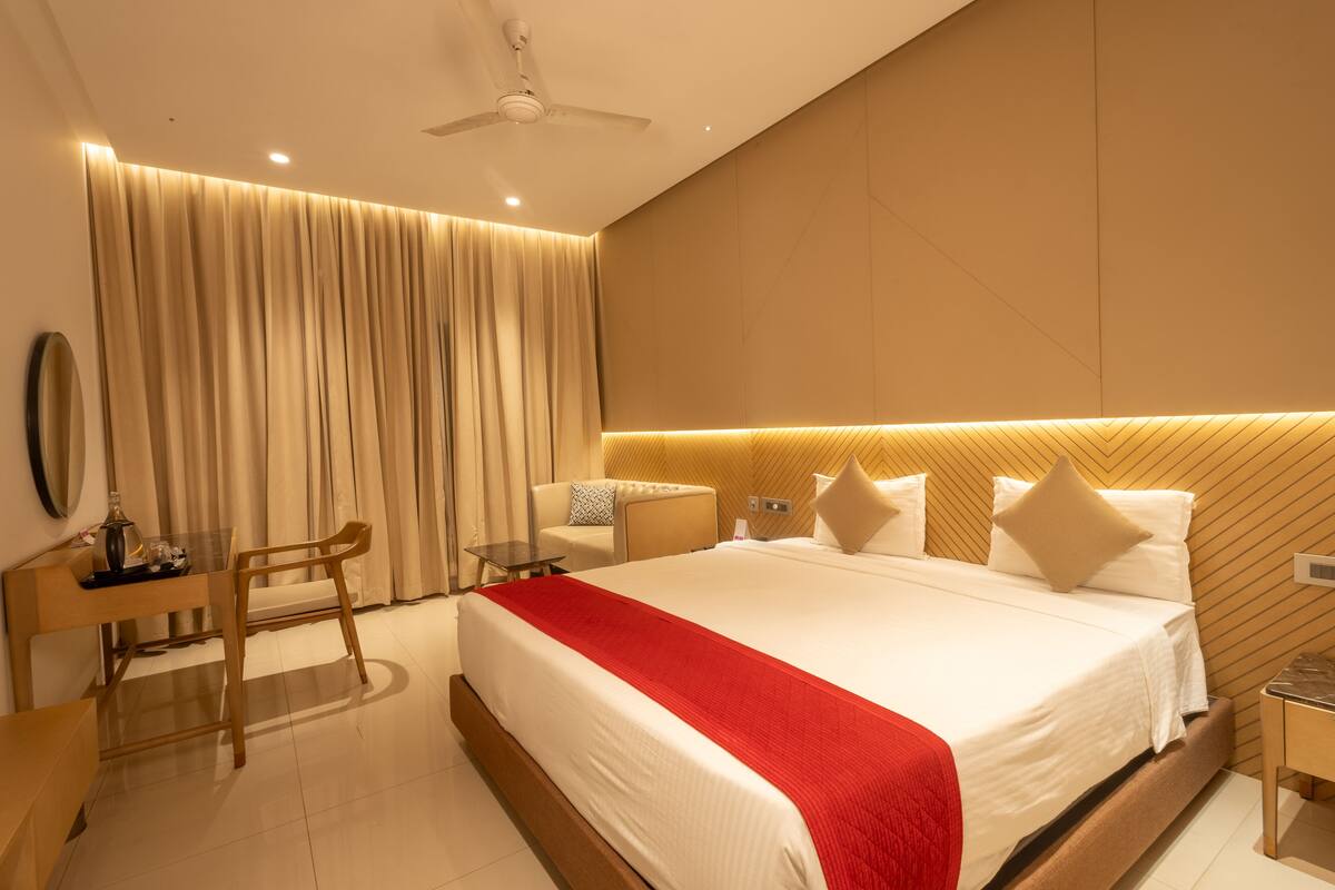 A modern hotel room with a large bed, a desk, a chair, and a nightstand.