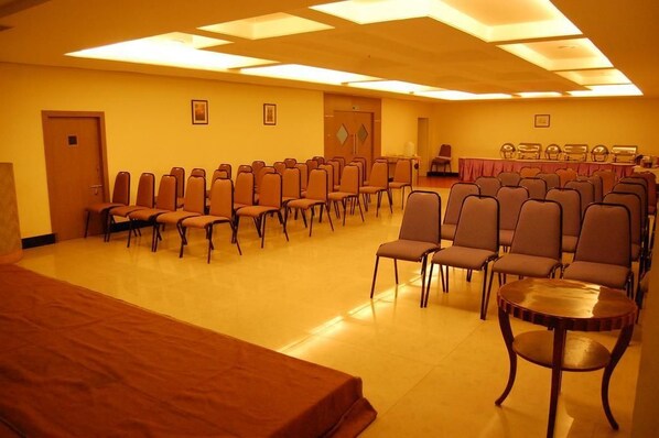 A conference room with rows of chairs, a long table, and a stage area. - Parsons Court (Thindukkal)