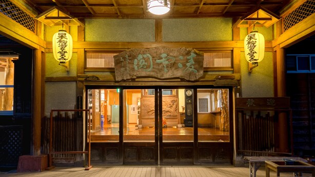Entrada de un edificio japonés tradicional con vigas de madera, suelo de baldosas y faroles.