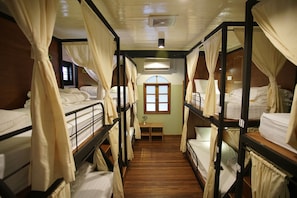 A room with bunk beds, wooden floors, a small table with a vase, and a window with curtains. - 501 Merchant Bed & Breakfast - Hostel (Yangon)