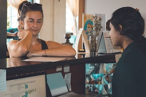 A reception desk with a computer monitor displaying a scheduling interface, a vase with dried flowers, and a calendar on the wall. - 501 Merchant Bed & Breakfast - Hostel (Yangon)