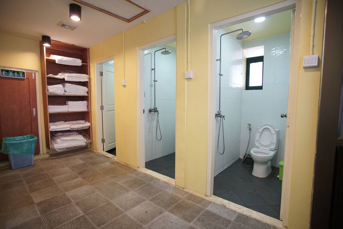 A public restroom with multiple shower stalls, a toilet, and a towel rack with folded towels.