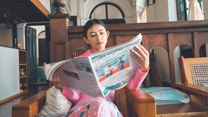 A person sitting on a wooden bench reading a newspaper. - 501 Merchant Bed & Breakfast - Hostel (Yangon)
