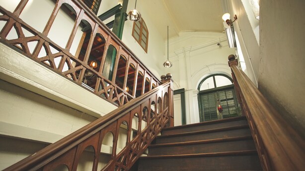 A wooden staircase with ornate railings and a view of a green door at the top. - 501 Merchant Bed & Breakfast - Hostel (Yangon)