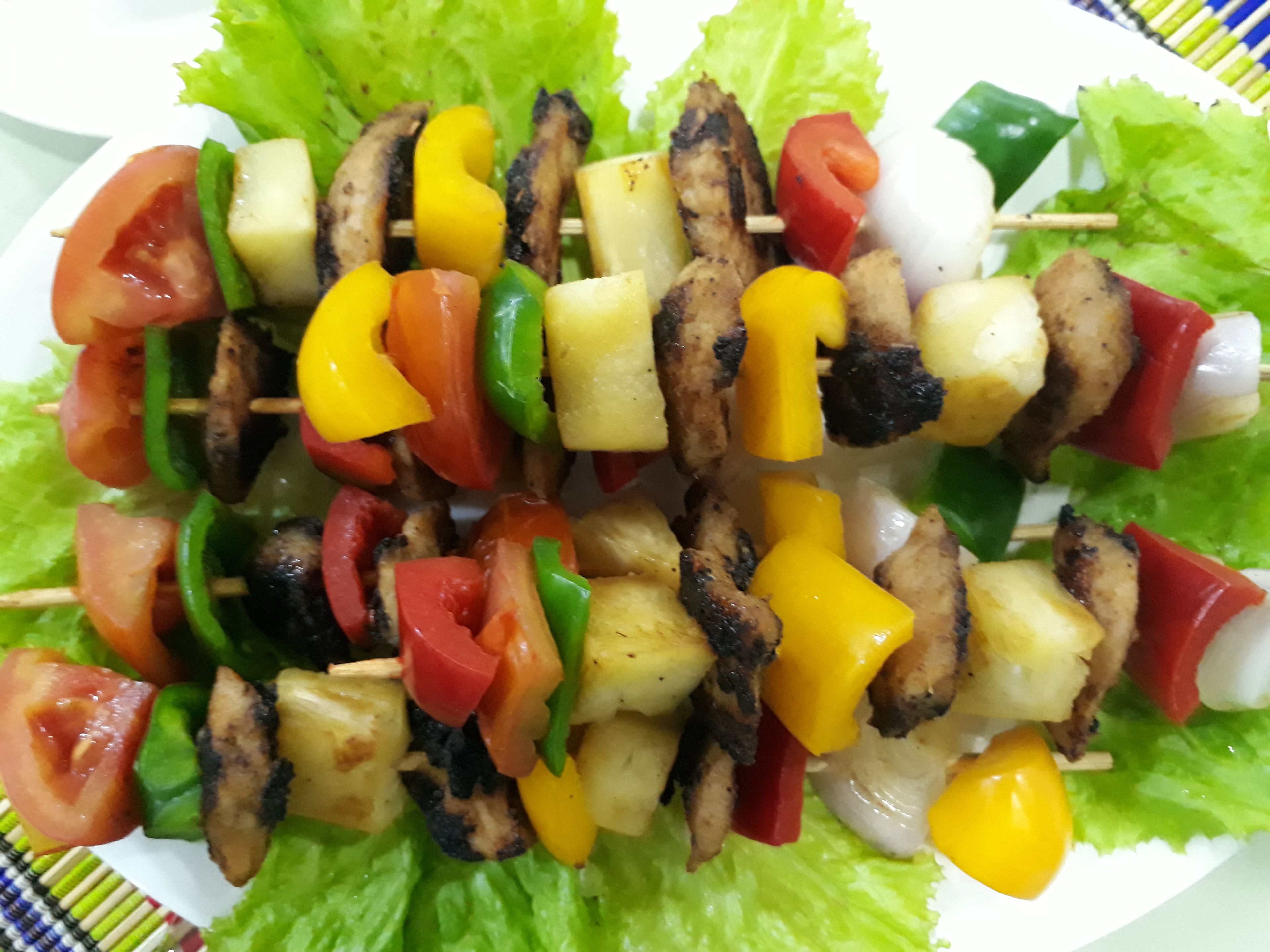 Um prato com espetos de legumes e carne grelhada, servido sobre uma cama de alface.