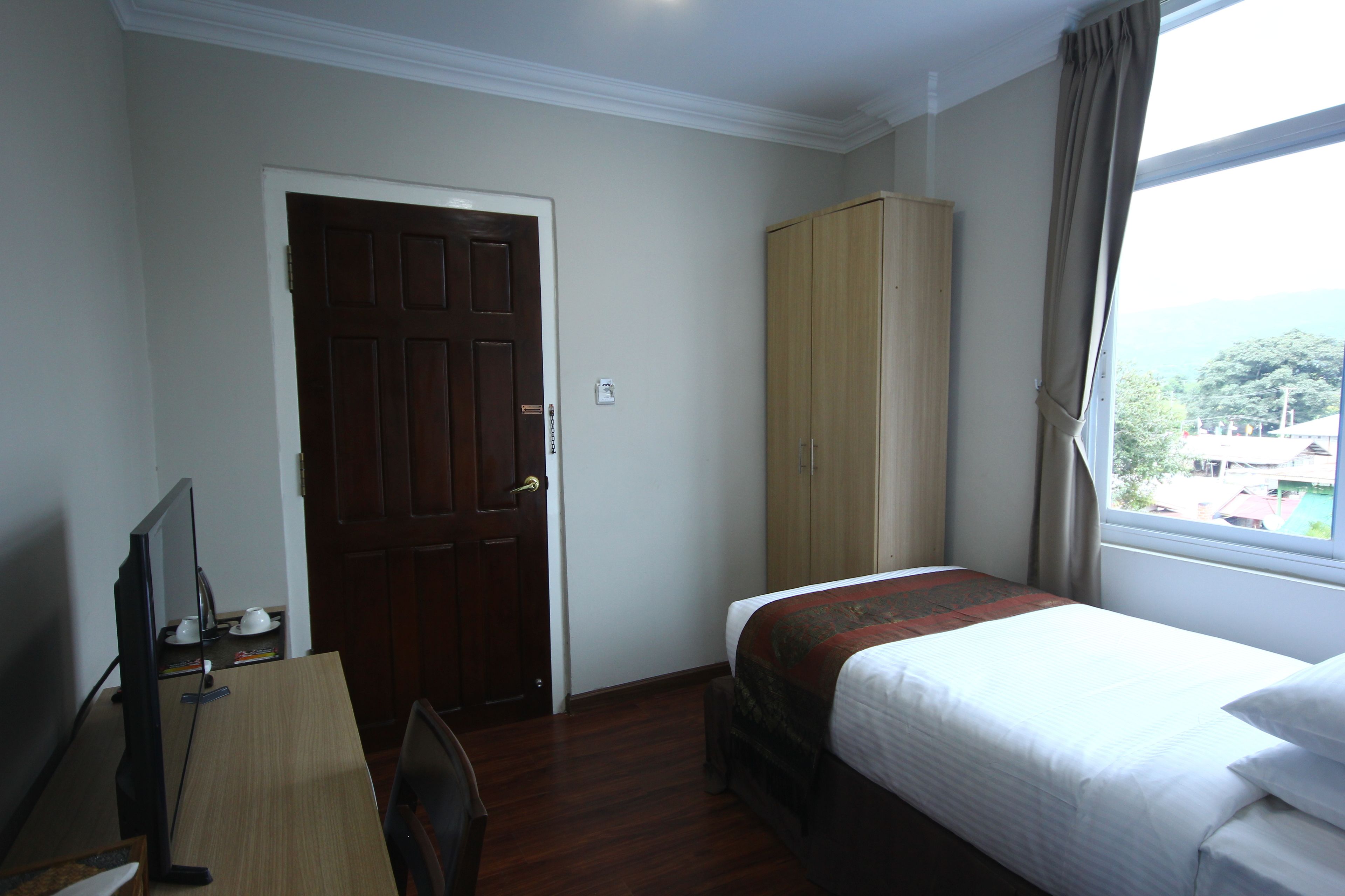 Una habitación de hotel con cama, escritorio con computadora, armario y ventana con cortinas.