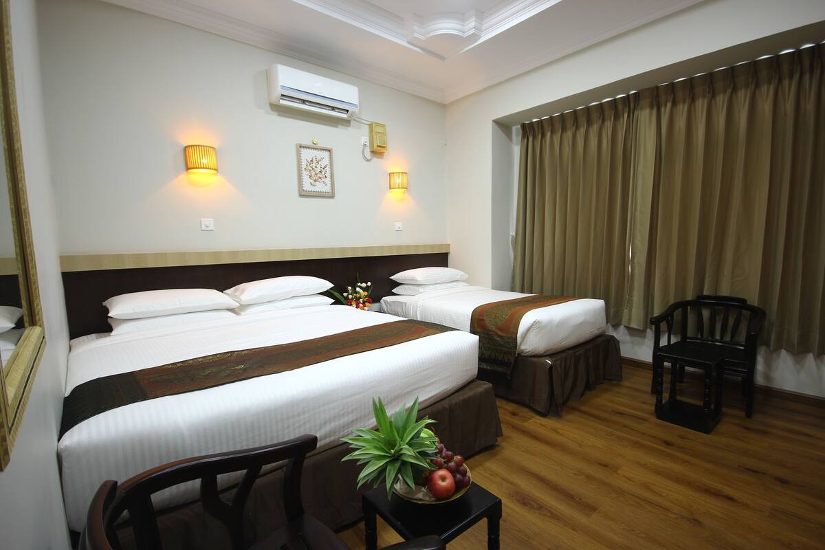 A hotel room with two beds, a wooden floor, a small table with fruit, and a chair.