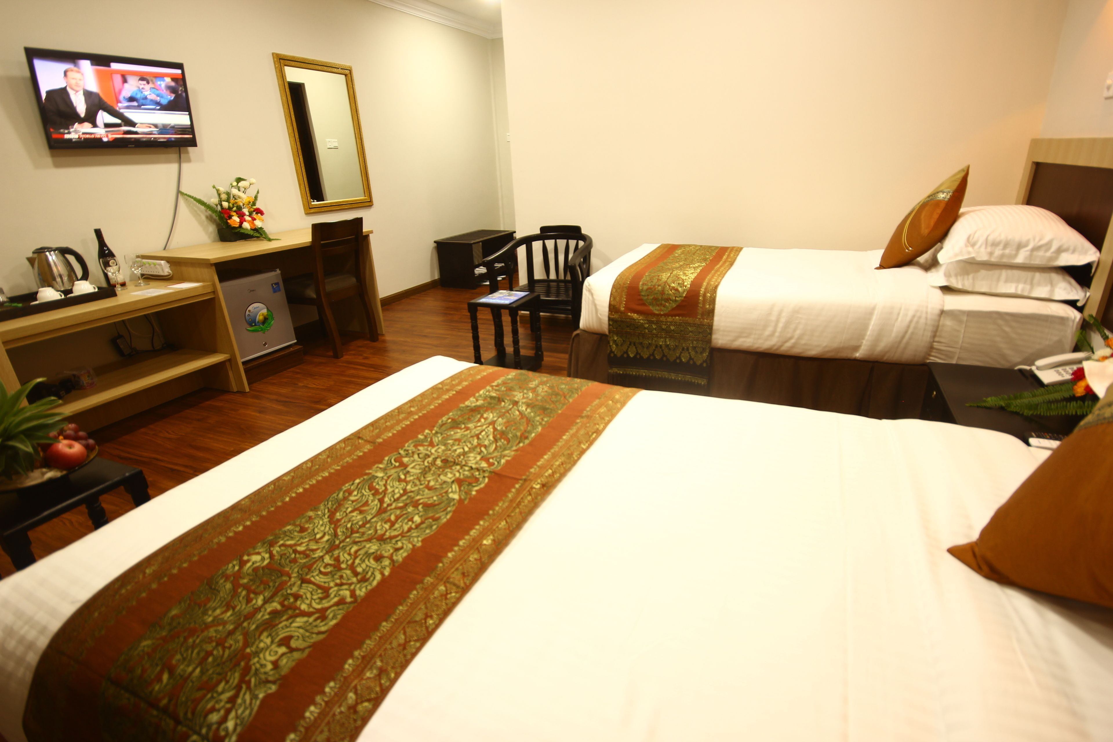 A hotel room with two beds, a desk with a computer, a chair, a television, and a small table with a plant.