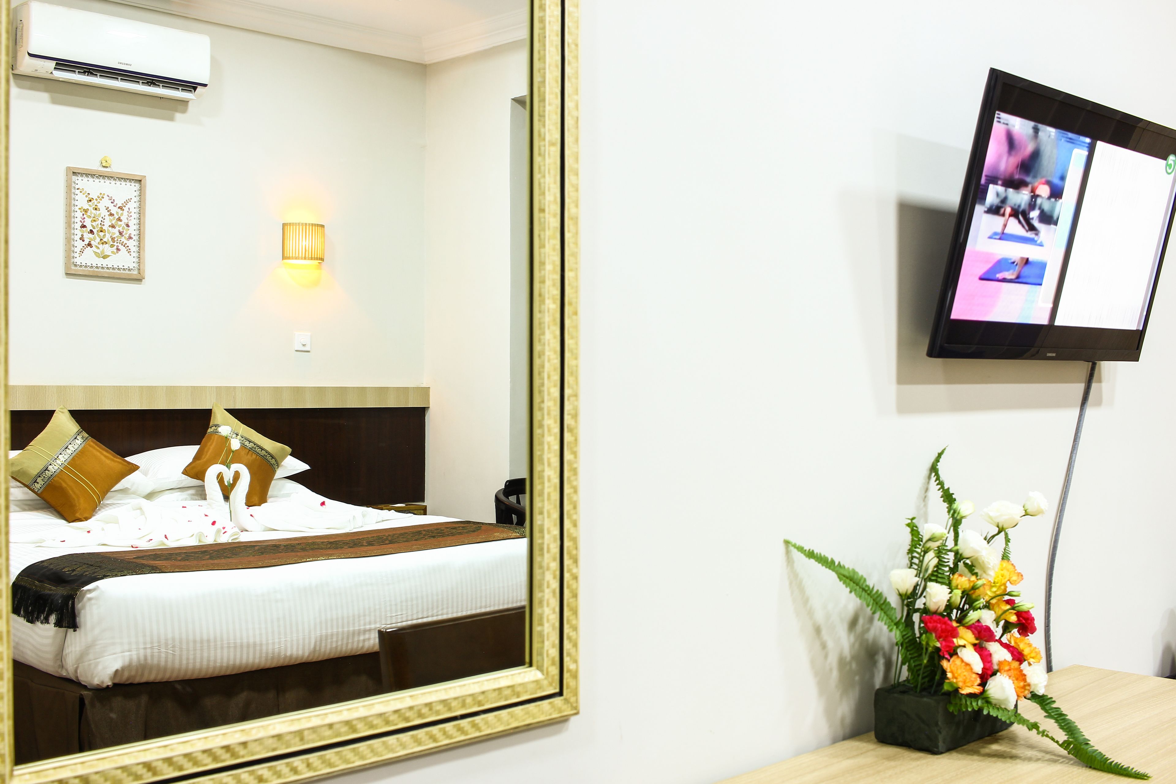 Una camera d'albergo con un letto, un grande specchio, una TV a muro e una pianta decorativa.