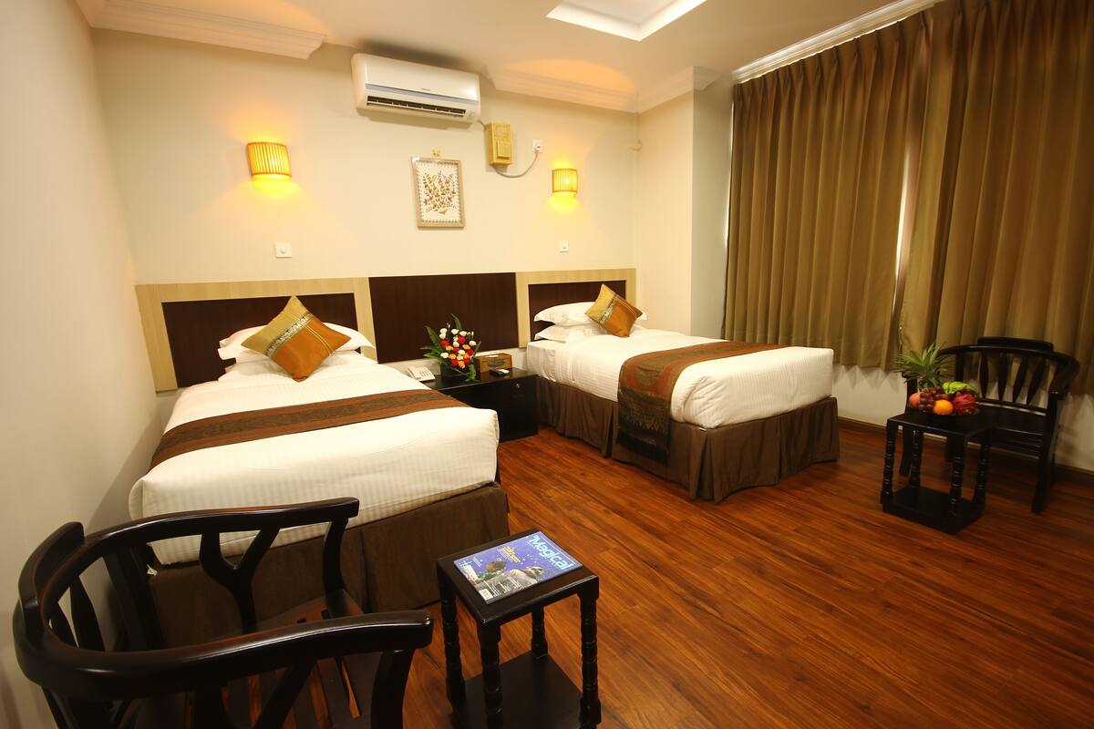A hotel room with two beds, a small table with a magazine, a chair, and a plant.