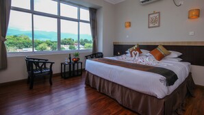A hotel room with a large bed, two chairs, a small table with fruit, and a view of mountains through large windows. - Immana Grand Inle Hotel (Nyaungshwe)