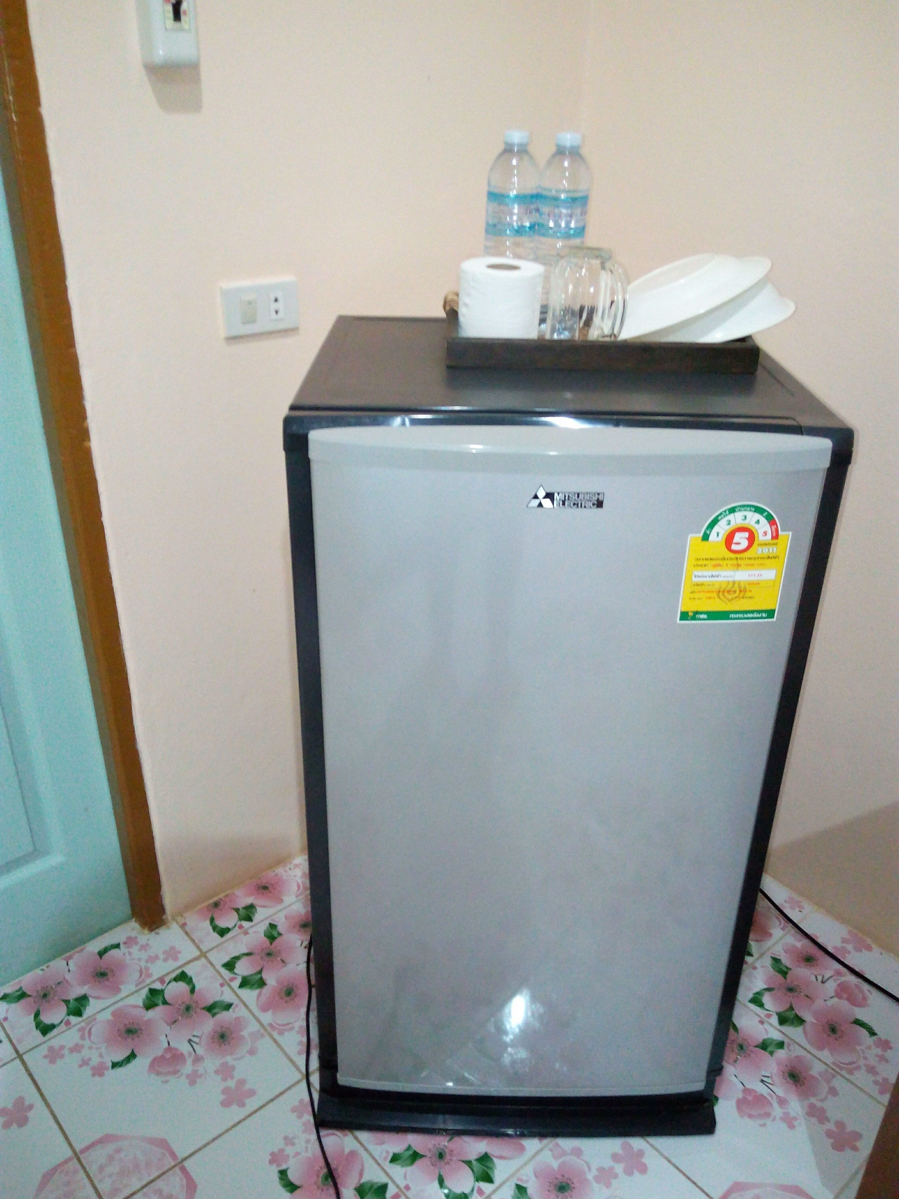 Un refrigerador compacto con el logotipo de Mitsubishi, un adhesivo que indica una garantía de 5 años y un dispensador de agua en la parte superior.