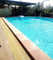 Piscina com borda azulejada, faixa de segurança emborrachada e área coberta com telhado.