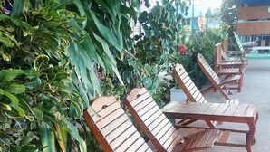 A row of wooden lounge chairs and tables arranged outdoors, surrounded by lush green foliage. - Peace Pool Resort (Khun Han)