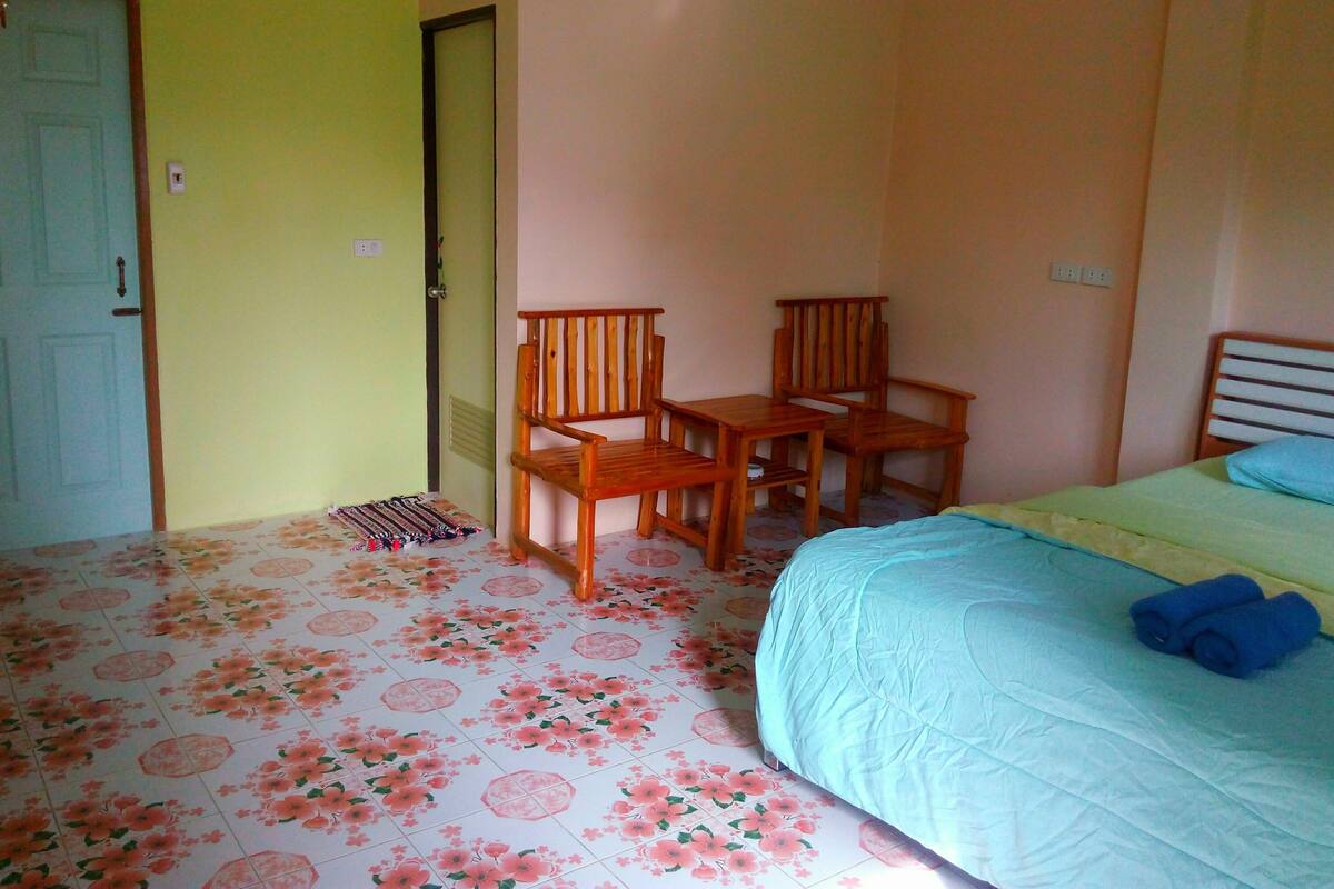 Ein Zimmer mit einem Bett, zwei Holzstühlen, einem kleinen Tisch und einer Tür.