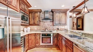 A modern kitchen with wooden cabinets, stainless steel appliances, a granite countertop, and a built-in oven. - Exclusive 2BR Ritz-Carlton w Mountain Rustic Décor by RedAwning - Save 20% on 7+ Nights! (Vail)