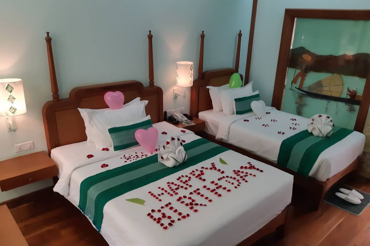 Ein Hotelzimmer mit zwei Betten, jeweils mit einer grün-weißen Streifenauflage, herzförmigen Kissen und einer 'Happy Birthday'-Aufschrift.