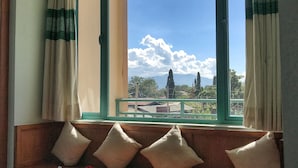 A room with a large window, a wooden bench with cushions, a table with a basket and a plate, and a view of the sky and distant landscape. - Nyaung Shwe City Hotel (Nyaungshwe)