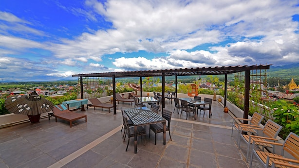 An outdoor patio with tables and chairs, a pergola, and a view of a cityscape and mountains. - Nyaung Shwe City Hotel (Nyaungshwe)