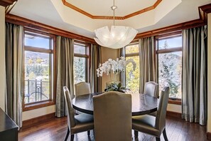 A dining room with a round table, four chairs, a chandelier, and large windows with curtains. - Chic 2 BR+Den Ritz-Carlton Condo with Valley Views by RedAwning - Save 20% on 7+ Nights! (Vail)