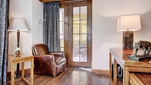 A room with a leather armchair, a wooden side table with a lamp, and a door leading outside. - Luxe 2BR+Den Ritz-Carlton Residence Quiet Location by RedAwning (Vail)
