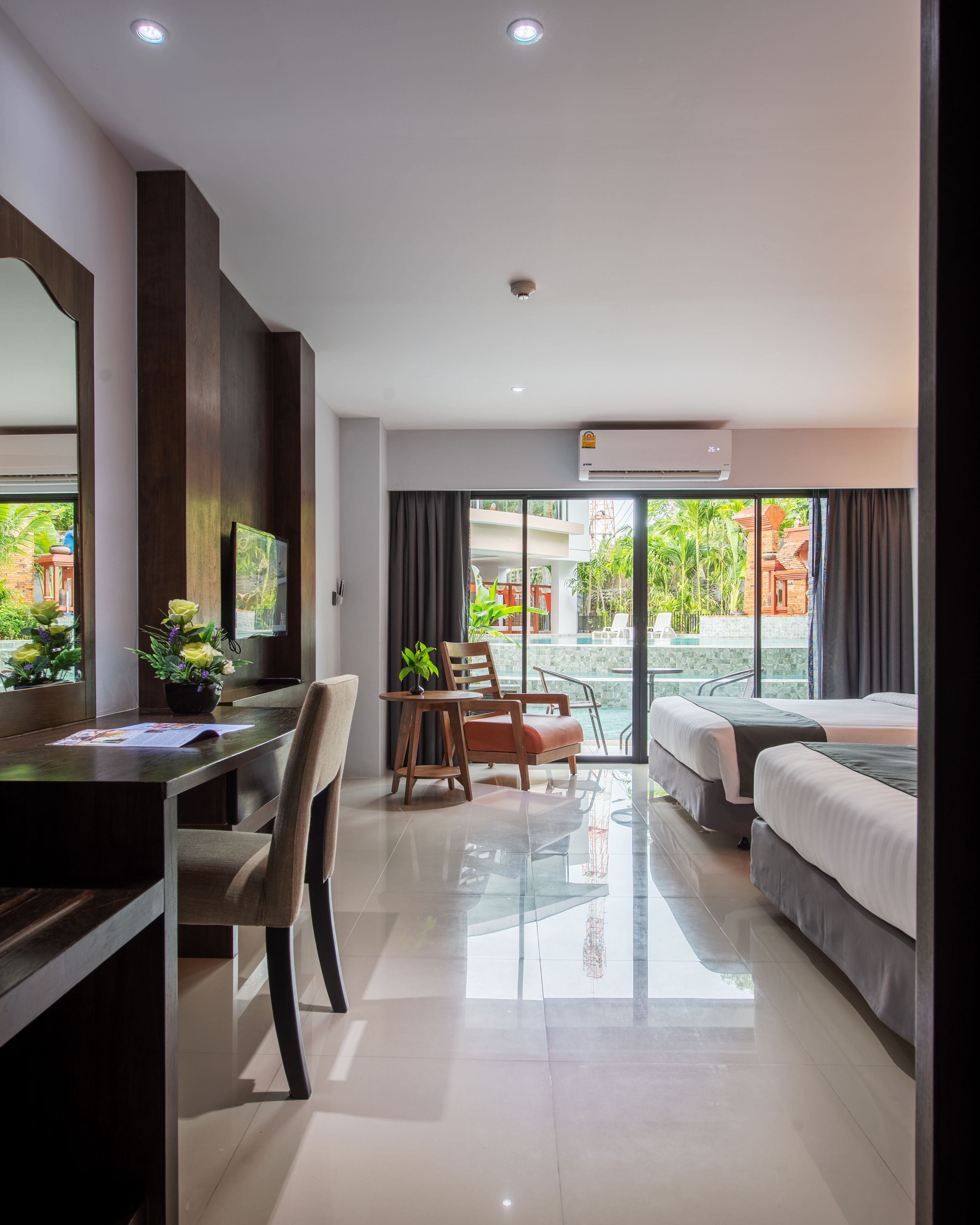 A modern hotel room with a desk, chairs, a bed, and a balcony with a pool view.