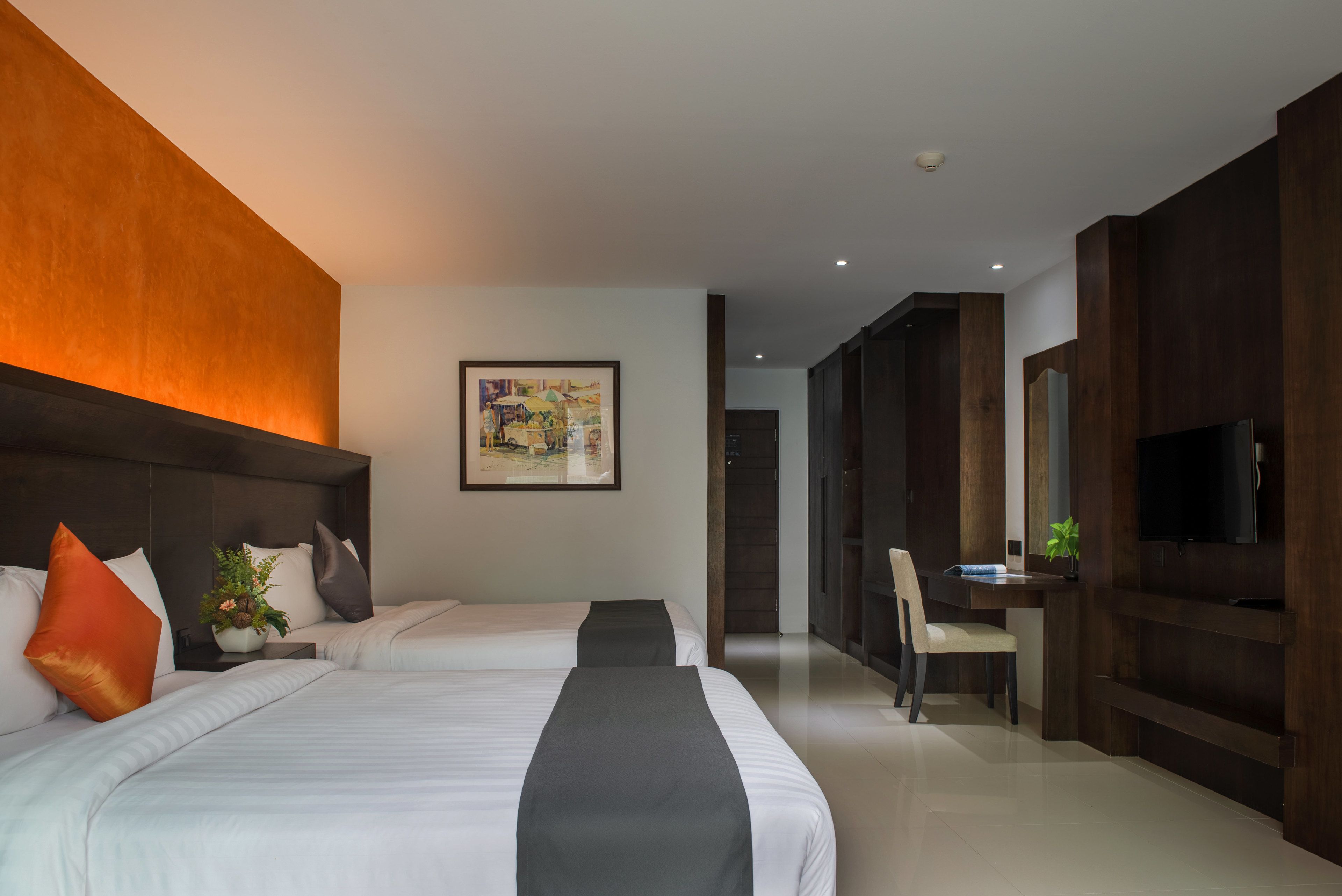 Habitación de hotel con dos camas, un escritorio, una silla, un televisor y un cuadro en la pared.