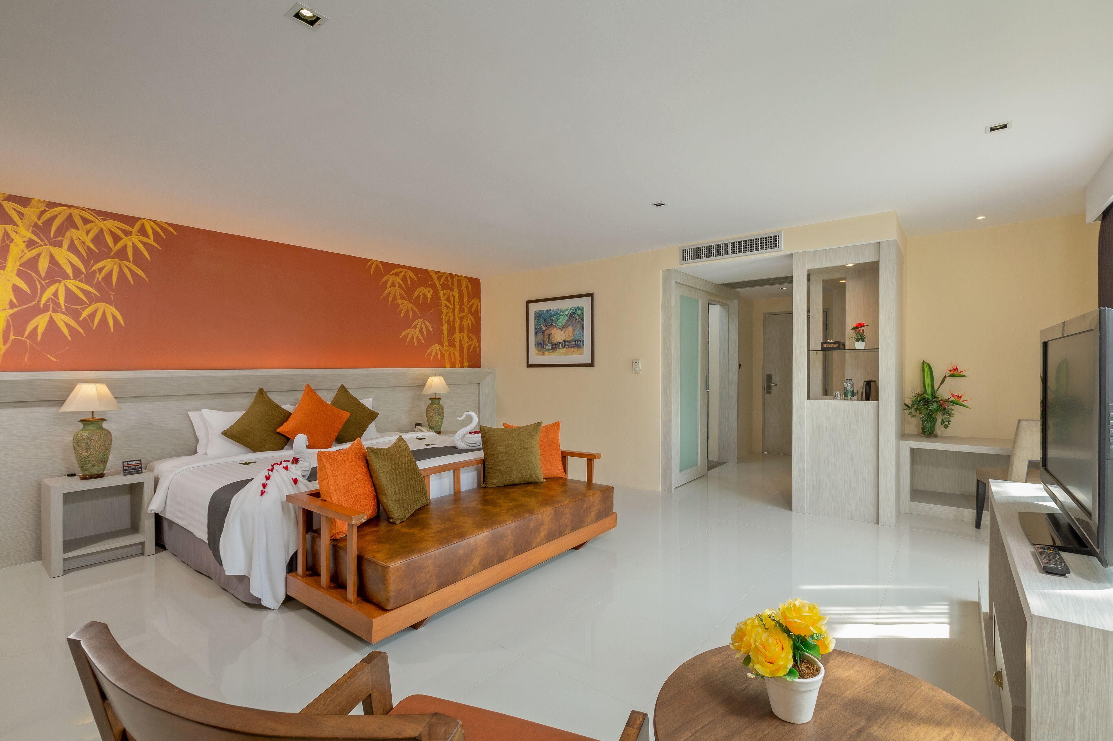 A modern hotel room with a bed, sofa, TV, and a dining area with a table and chairs.