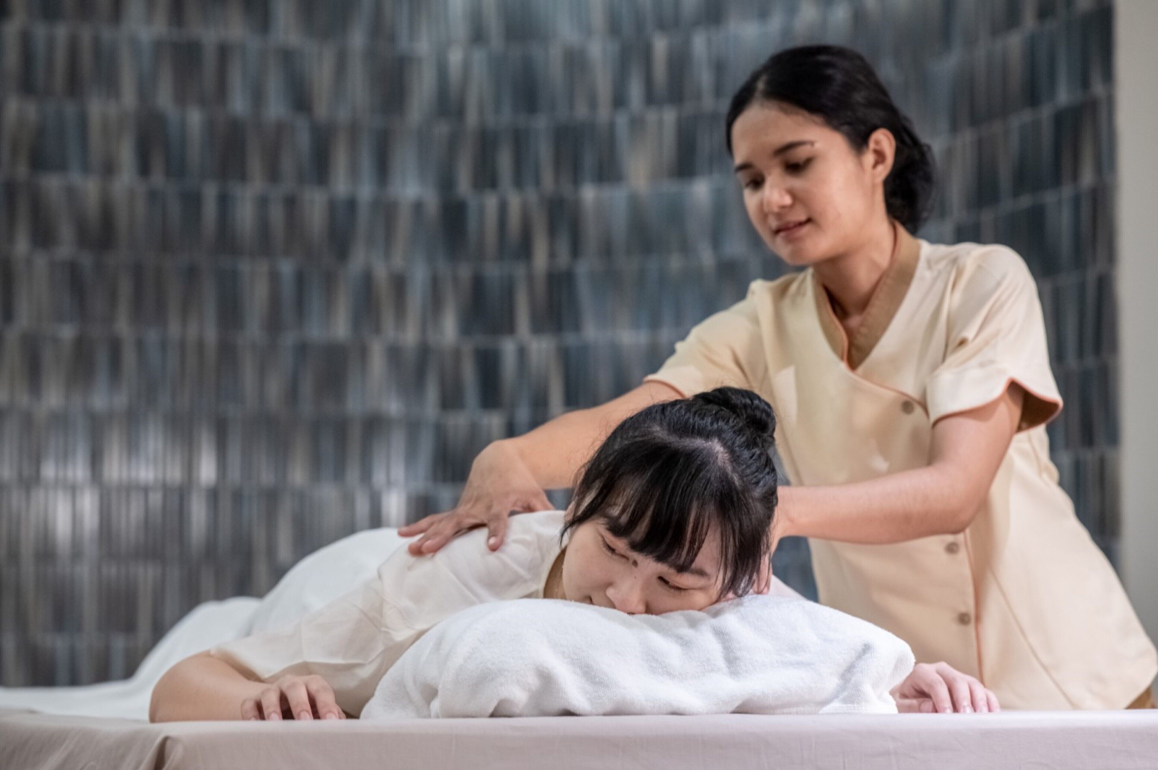 A person receiving a massage on a bed in a room with a textured wall.