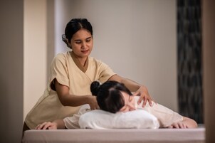 A massage therapy session in a room with a plain wall and a curtain.