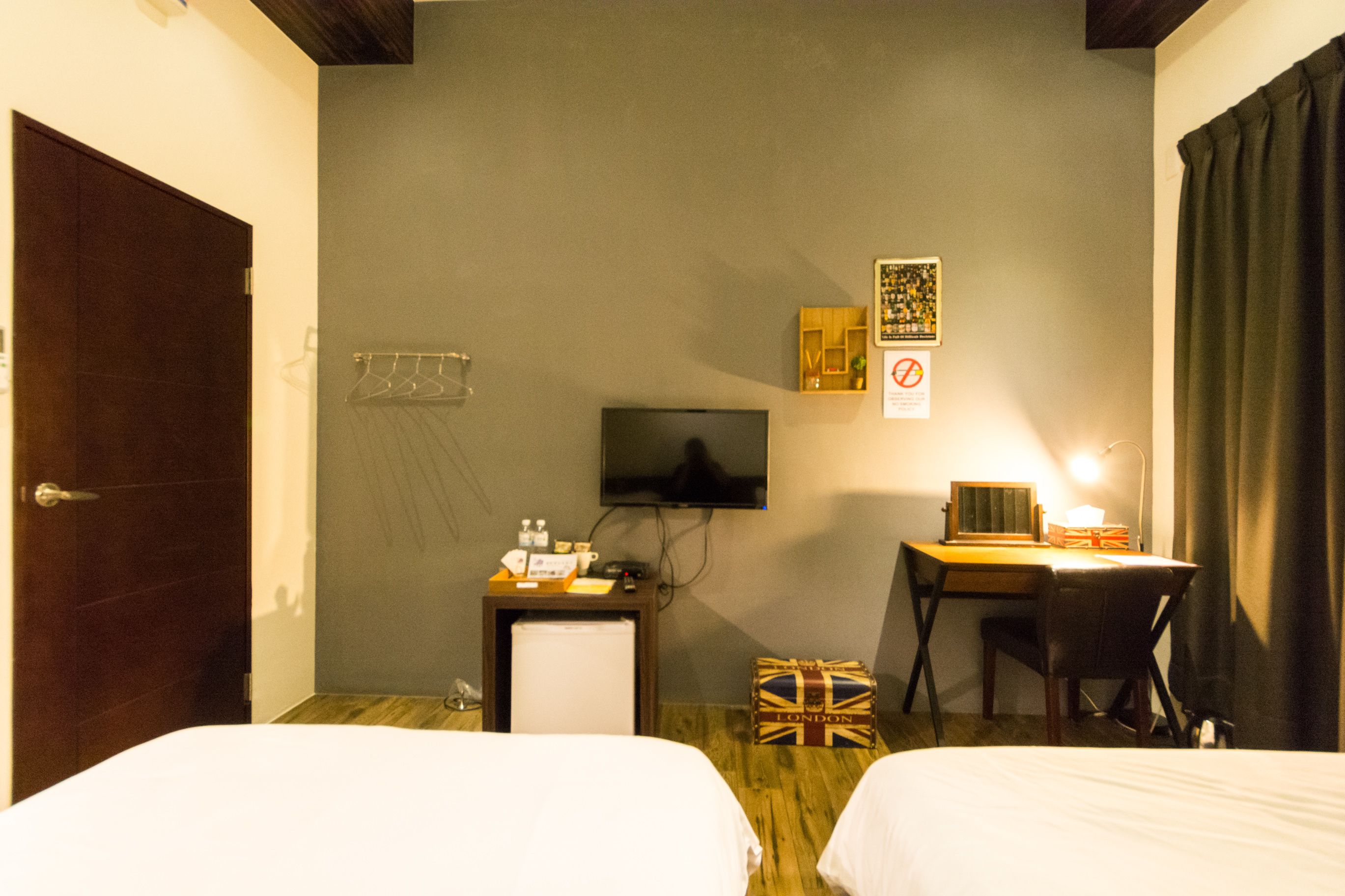 A hotel room with two beds, a desk, a television, a small refrigerator, and a suitcase.