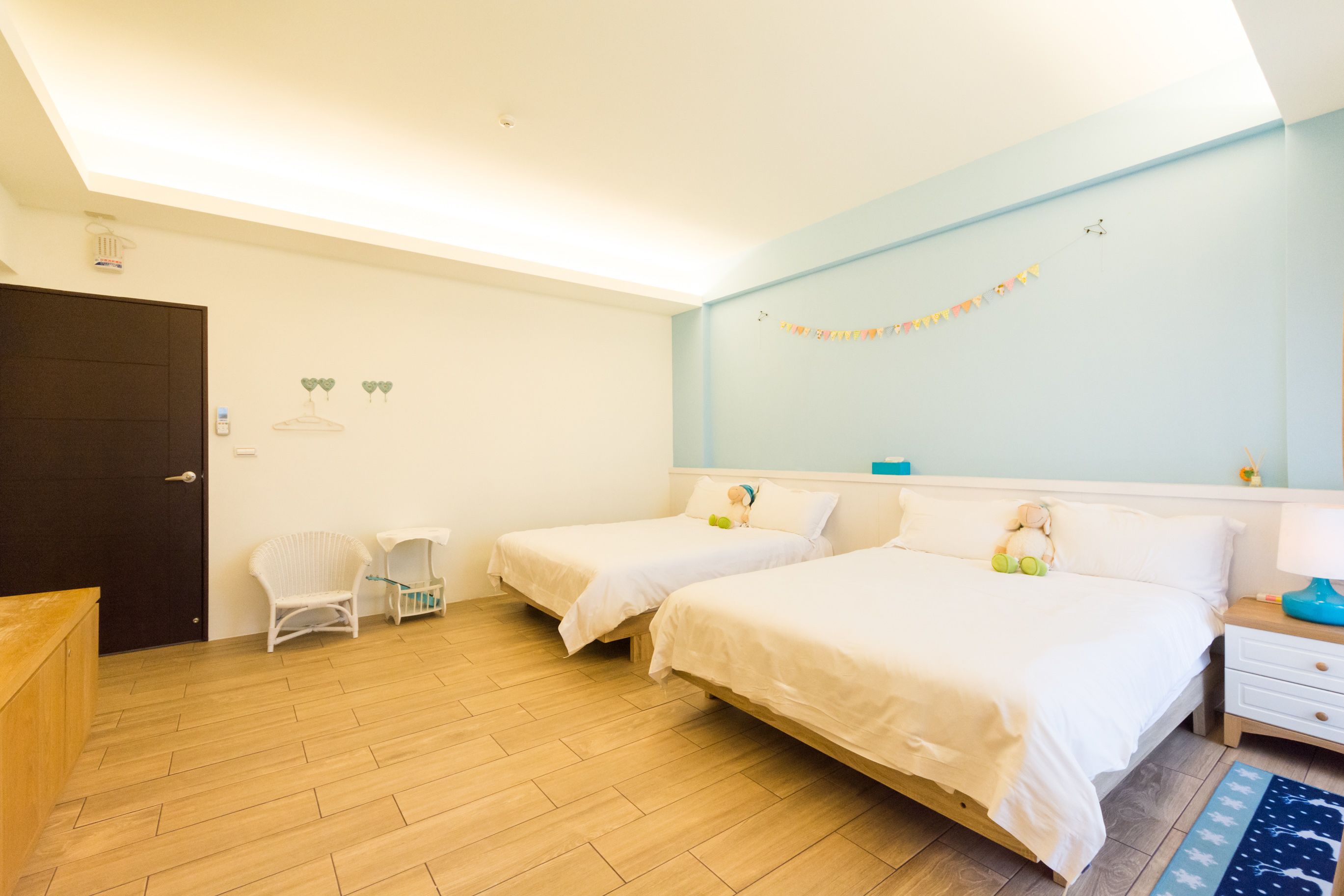 A bedroom with two beds, a wooden floor, a dark door, and a small white chair.
