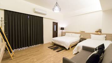 A hotel room with two beds, a sofa, a wooden floor, a black curtain, a lamp, and a hanging light fixture.