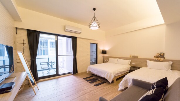 Habitación de hotel con dos camas, un sofá, un escritorio con una computadora portátil, un ventanal grande y un balcón.