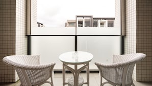 Un balcón con dos sillas de mimbre y una mesa de vidrio, con vistas a un edificio moderno.