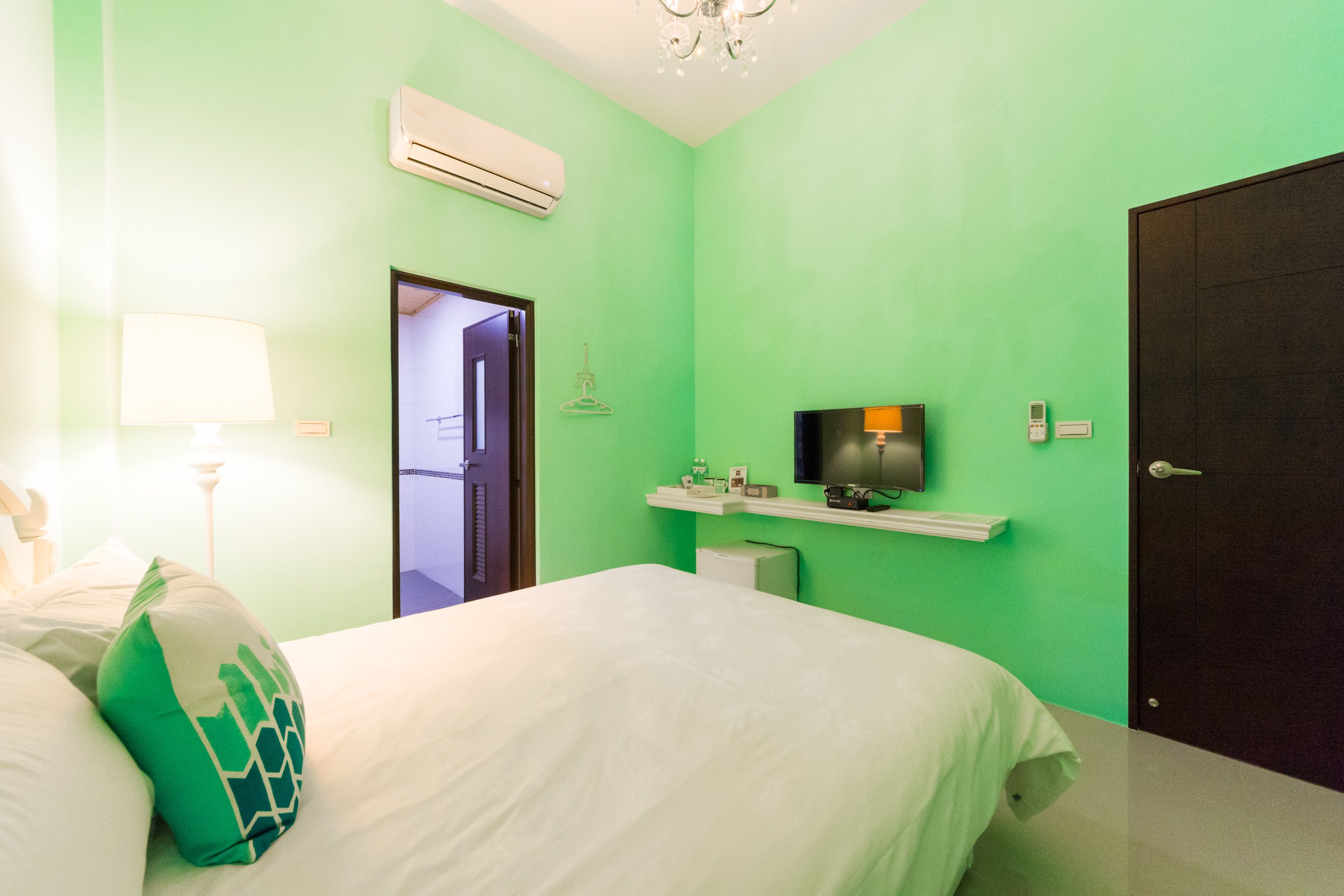 A room with a bed, a TV mounted on the wall, a door, and a wall-mounted air conditioner.