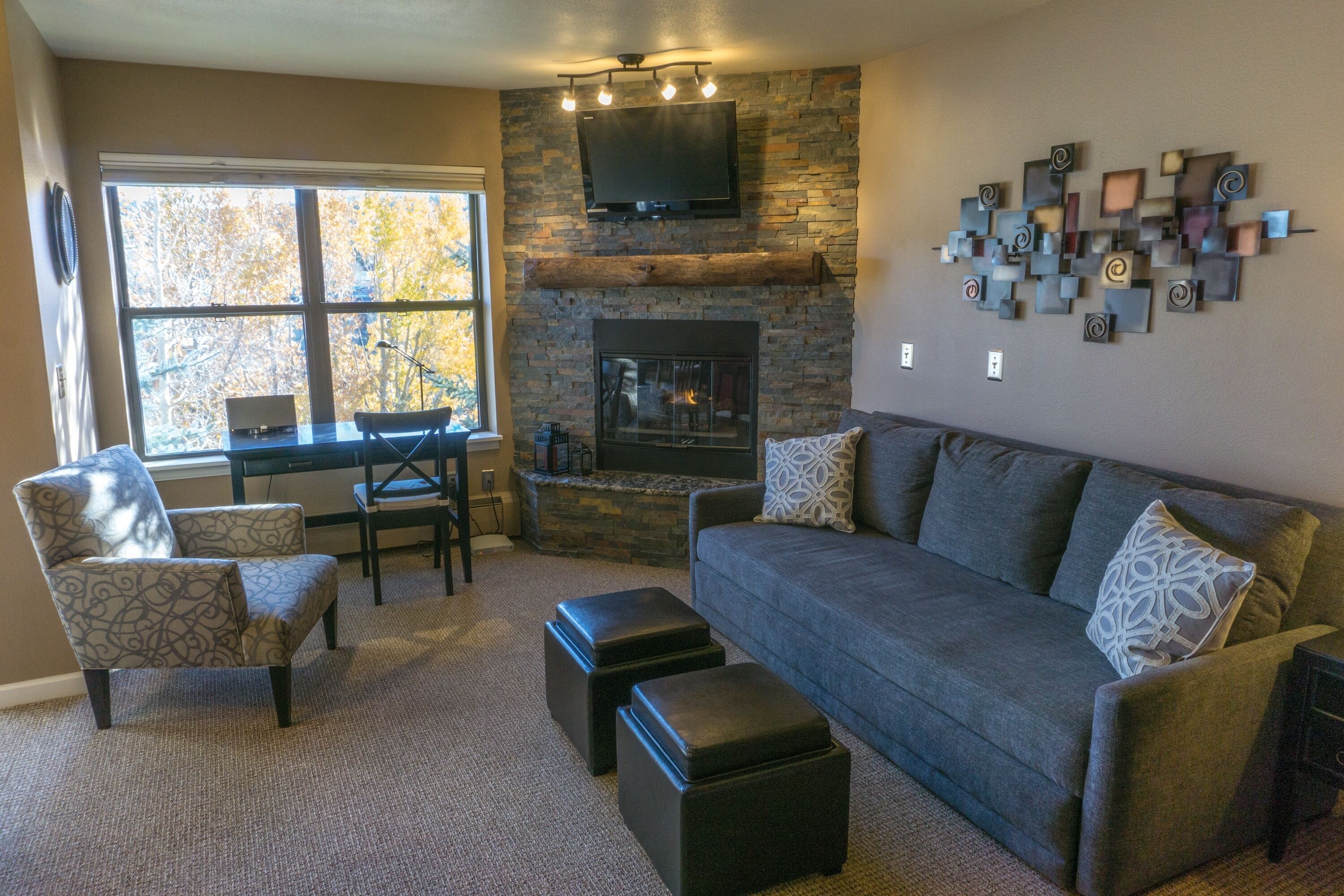 A living room with a stone fireplace, a television mounted above it, and a modern abstract art piece on the wall.