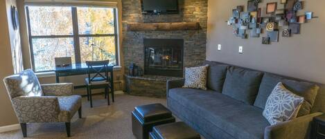 A living room with a stone fireplace, a television mounted above it, and a modern abstract art piece on the wall.