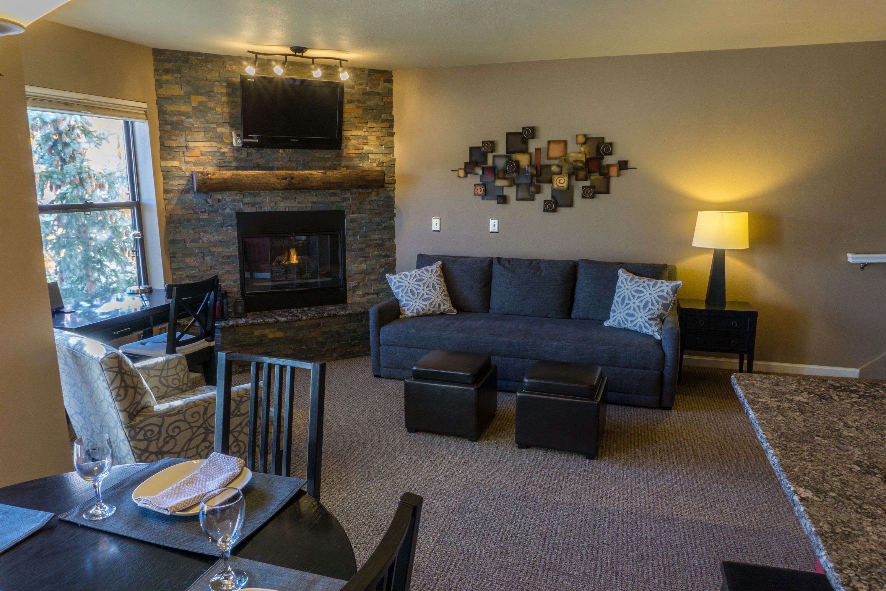 A living room with a stone fireplace, a sofa, a coffee table, and a TV mounted on the wall.