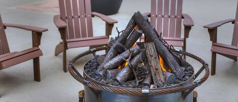 Una chimenea metálica con leña, rodeada de sillas Adirondack.