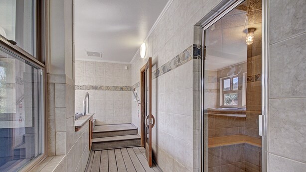 Ein modernes Badezimmer mit Duschkabine aus Glas, einer Holzbank und Blick ins Freie durch ein Fenster.