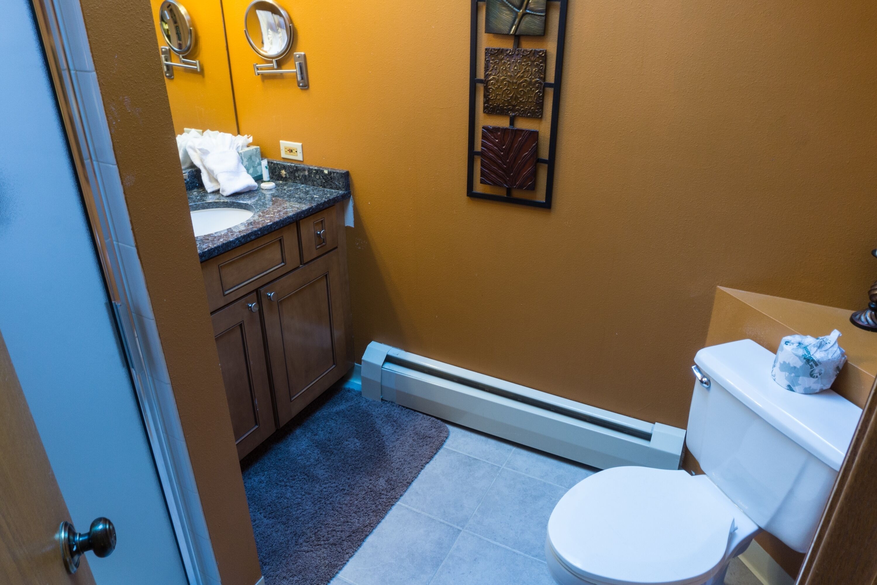 A compact bathroom with a white toilet, a sink, and a mirror. There is a towel rack with towels and a decorative wall piece above the sink.