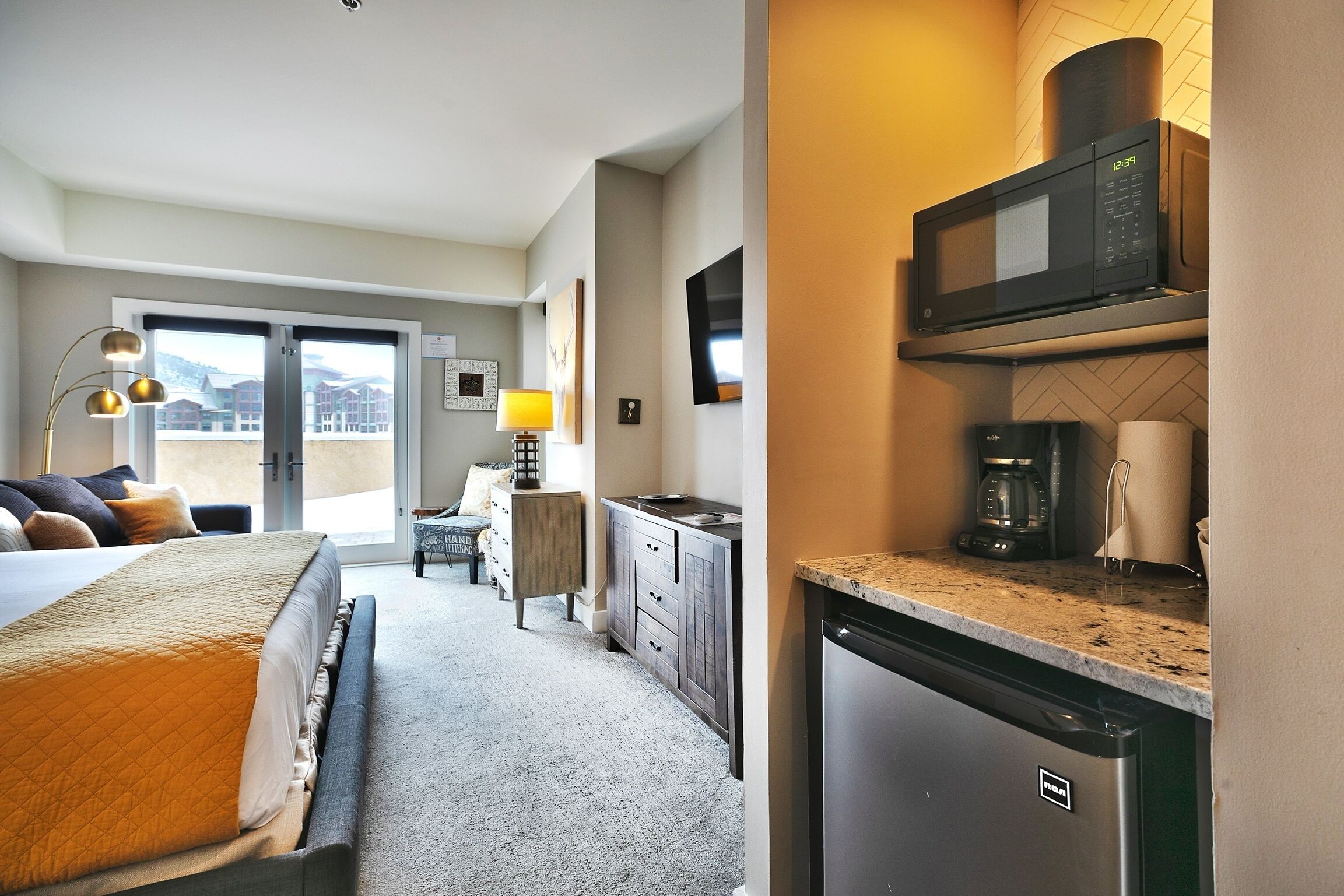 A hotel room with a bed, a desk, a microwave, a coffee maker, and a dishwasher.
