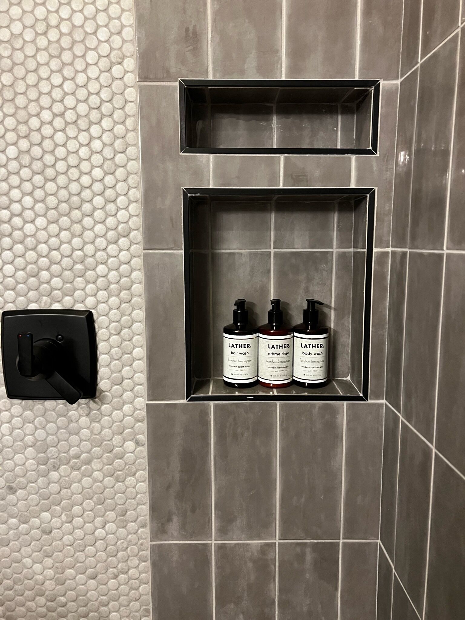 Casa de banho com parede revestida em azulejo, secador de mãos e três produtos Lather para o cabelo.